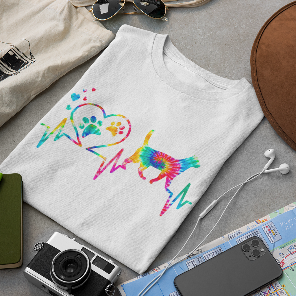 White t-shirt with colorful graphic design on a gray surface with accessories like a camera, hat, and map.