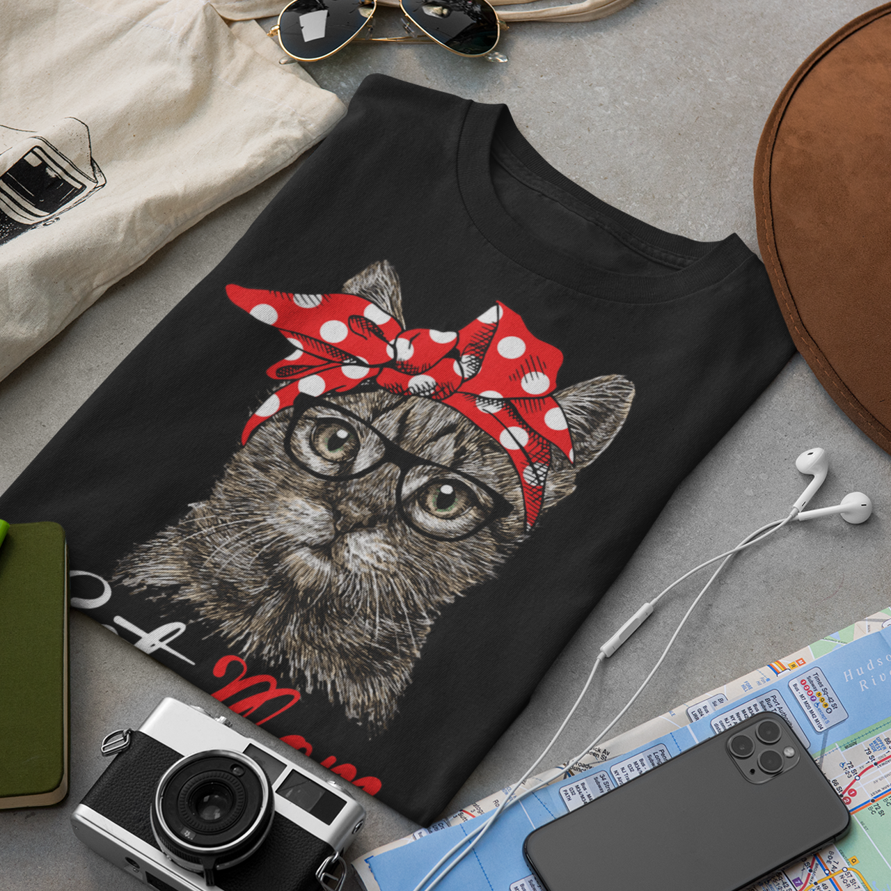 Black tank top with a cat design wearing a red bandana, surrounded by sunglasses, camera, map, and other items on a gray surface.