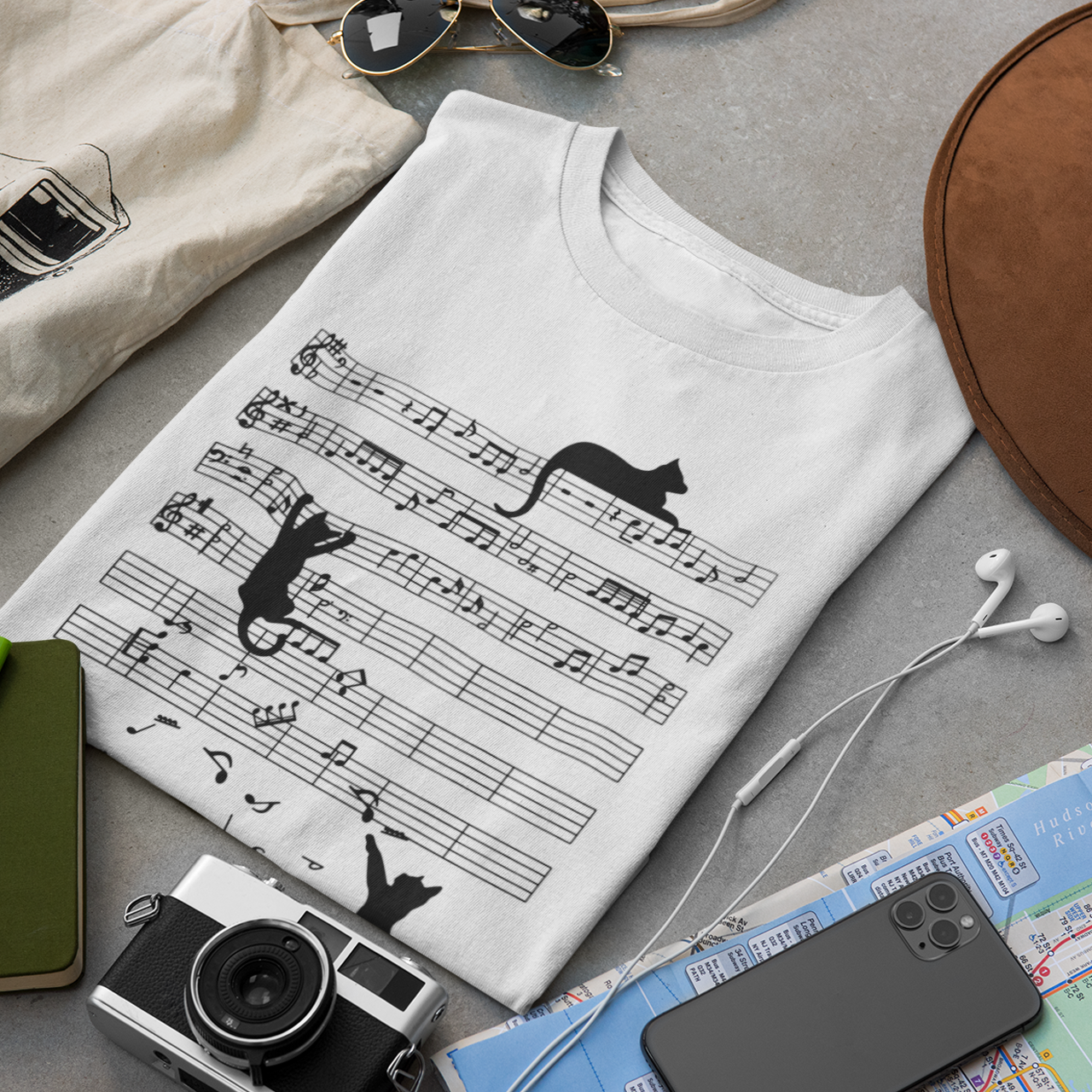 White t-shirt with music sheet design, camera, hat, notebook, and phone on a gray surface